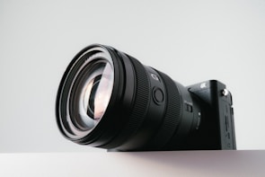 A modern DSLR camera with a large lens against a soft blurred background.