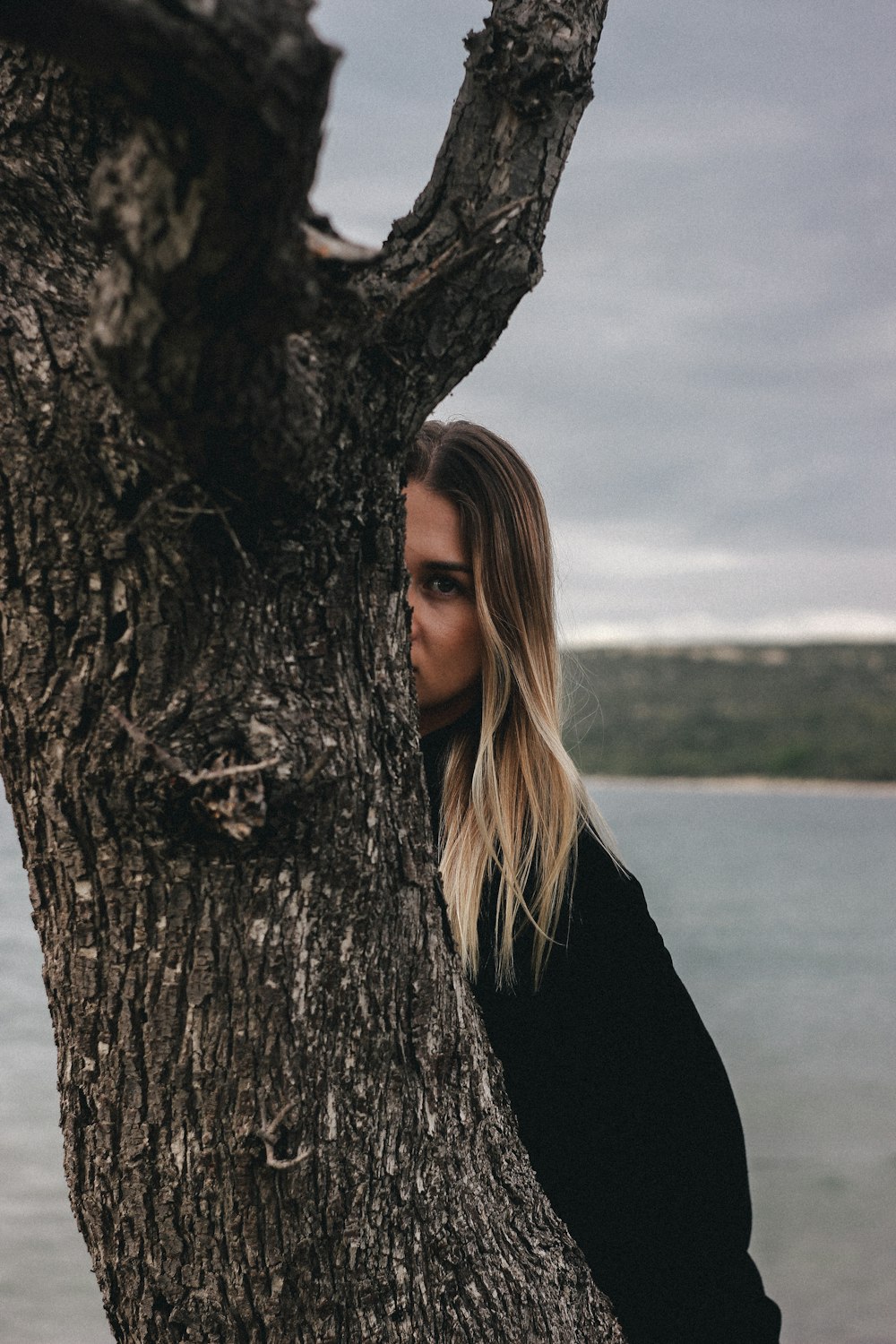 a woman standing next to a tree near a body of water