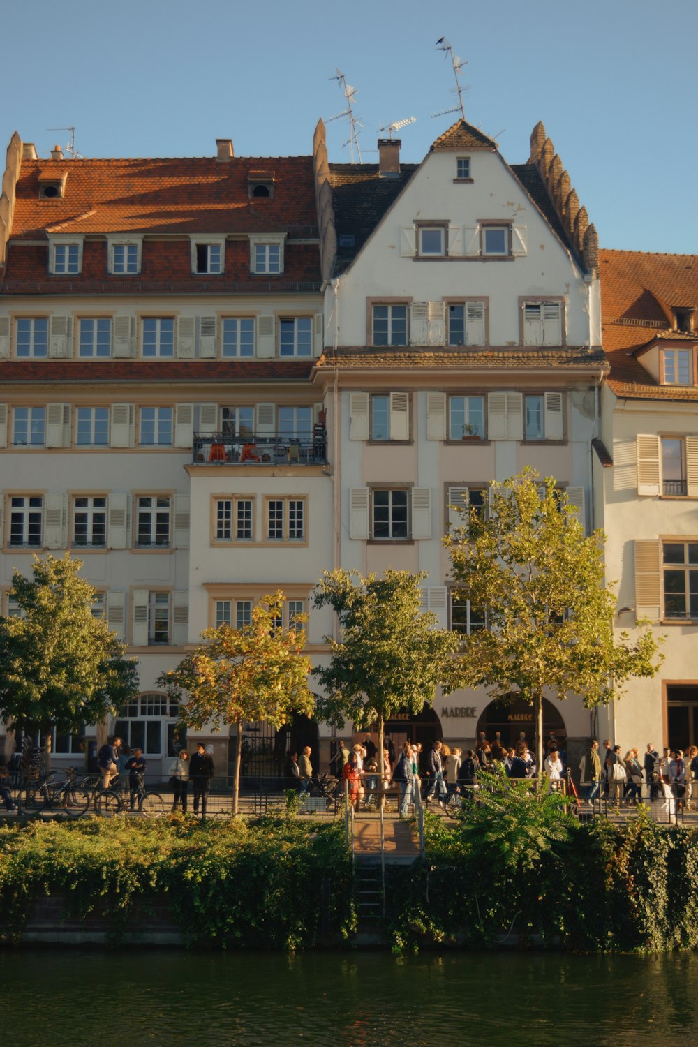 a group of people standing in front of a building next to a body of water