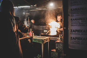 Street vendor expertly flipping roti canai on a hot griddle with flames flickering