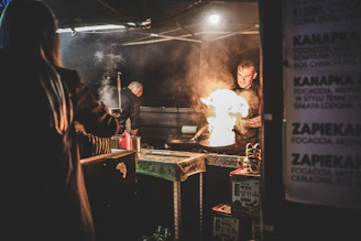 Street vendor expertly flipping roti canai on a hot griddle with flames flickering