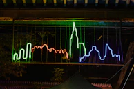 A glowing neon sign of the eternal vibe chronicles logo illuminating a nighttime cityscape.