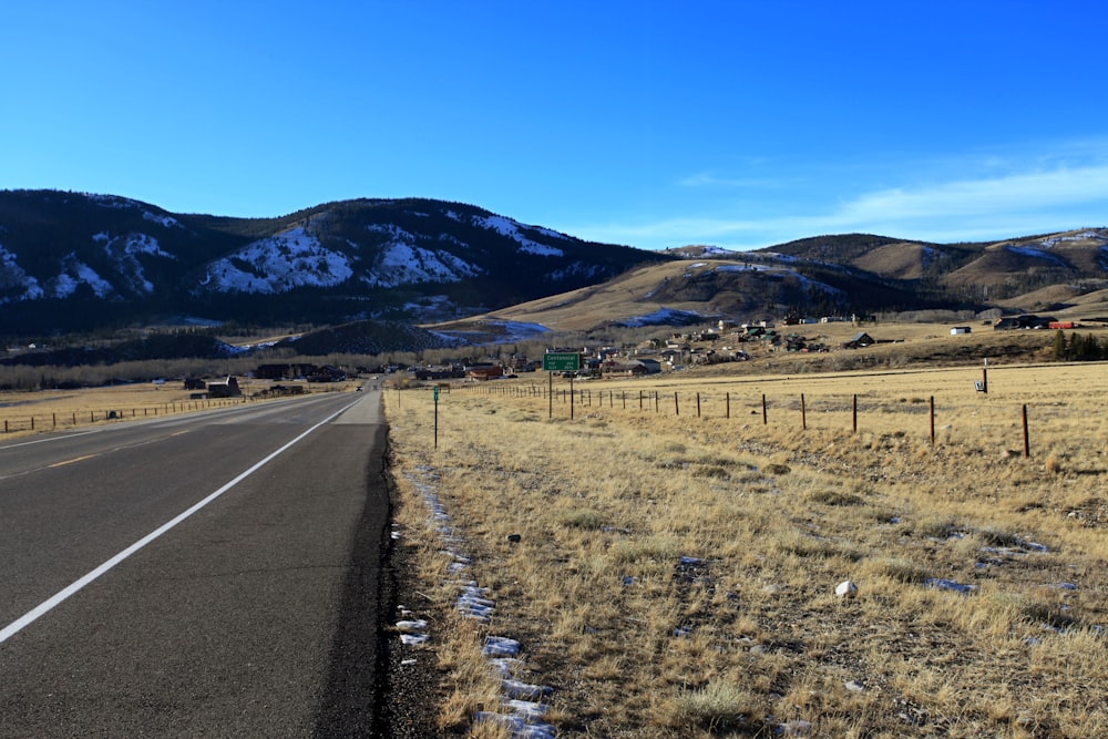 a road in the middle of a field with mountains in the background