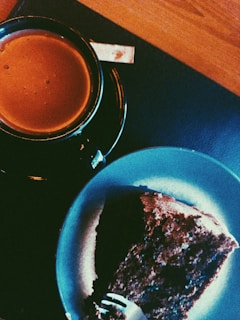A warm cup of coffee next to a piece of cake.