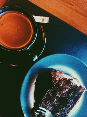 A steaming cup of coffee beside a decadent slice of cake.