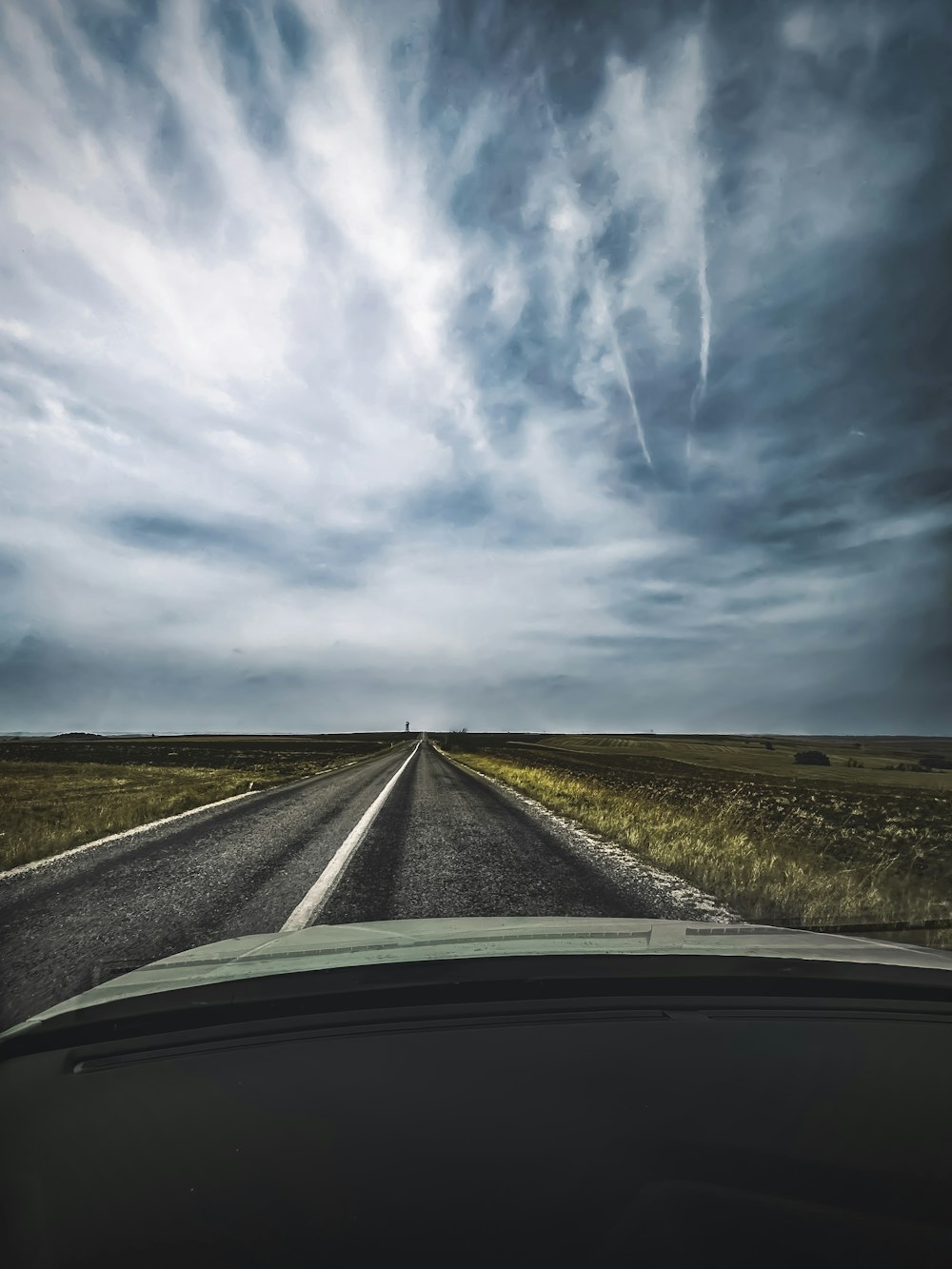 a car driving down an empty road under a cloudy sky