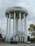 A tall, cylindrical water tower with the word 'Toronto' painted in blue at the top stands prominently against a cloudy sky. The structure is supported by multiple vertical pillars. In the foreground, there are a few leafless trees, two parked cars, and a brick building partially visible on the left side. The surrounding area is fenced, with some autumnal trees showing yellow and brown leaves.