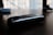 A harmonica rests on a wooden surface in a dimly lit room. The focus is on the instrument, with a blurred background suggesting an urban setting seen through a window. The metallic surface of the harmonica reflects some of the available light, adding a subtle sheen.