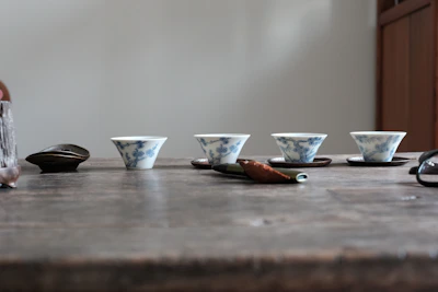 Close-up of elegant Chinese-style ceramic tea cups and saucers with delicate patterns on a wooden table.