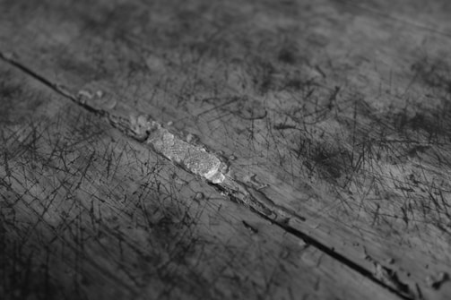 A close-up of a textured surface with numerous scratches and a visible crack running diagonally across. The surface appears worn and rugged, suggesting possible use over time or harsh conditions.