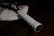 A close-up view of a tennis racket handle resting on what appears to be a white fabric. The focus is on the handle's grip, which is white and textured, contrasting against the dark background.