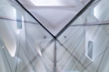 An abstract architectural structure featuring intersecting lines and reflective surfaces, creating a symmetrical pattern. The image incorporates translucent elements and soft gradients, contributing to a futuristic and minimalist design aesthetic.