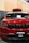 A front view of a customized red SUV with black accents. The car has a prominent grille with multiple horizontal slots, a hood scoop, and a roof-mounted cargo box. The windshield has decals, including 'STNCSG,' and a piece of paper placed on the dashboard. The background includes a wall with vertical wooden panels and part of a ceiling structure.