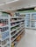 The image depicts the interior of a convenience store with neatly arranged shelves filled with various snacks, packaged foods, and beverages. There are several refrigerated sections visible in the background, stocked with drinks and dairy products. The store appears to be well-lit with a clean and organized layout.