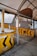 A weathered, enclosed structure featuring several yellow barriers with black arrow markings. The barriers are rusted, and there are various signs in a non-English language. The area appears to be an old or abandoned checkpoint or toll booth with metal frames and a faded roof covering.