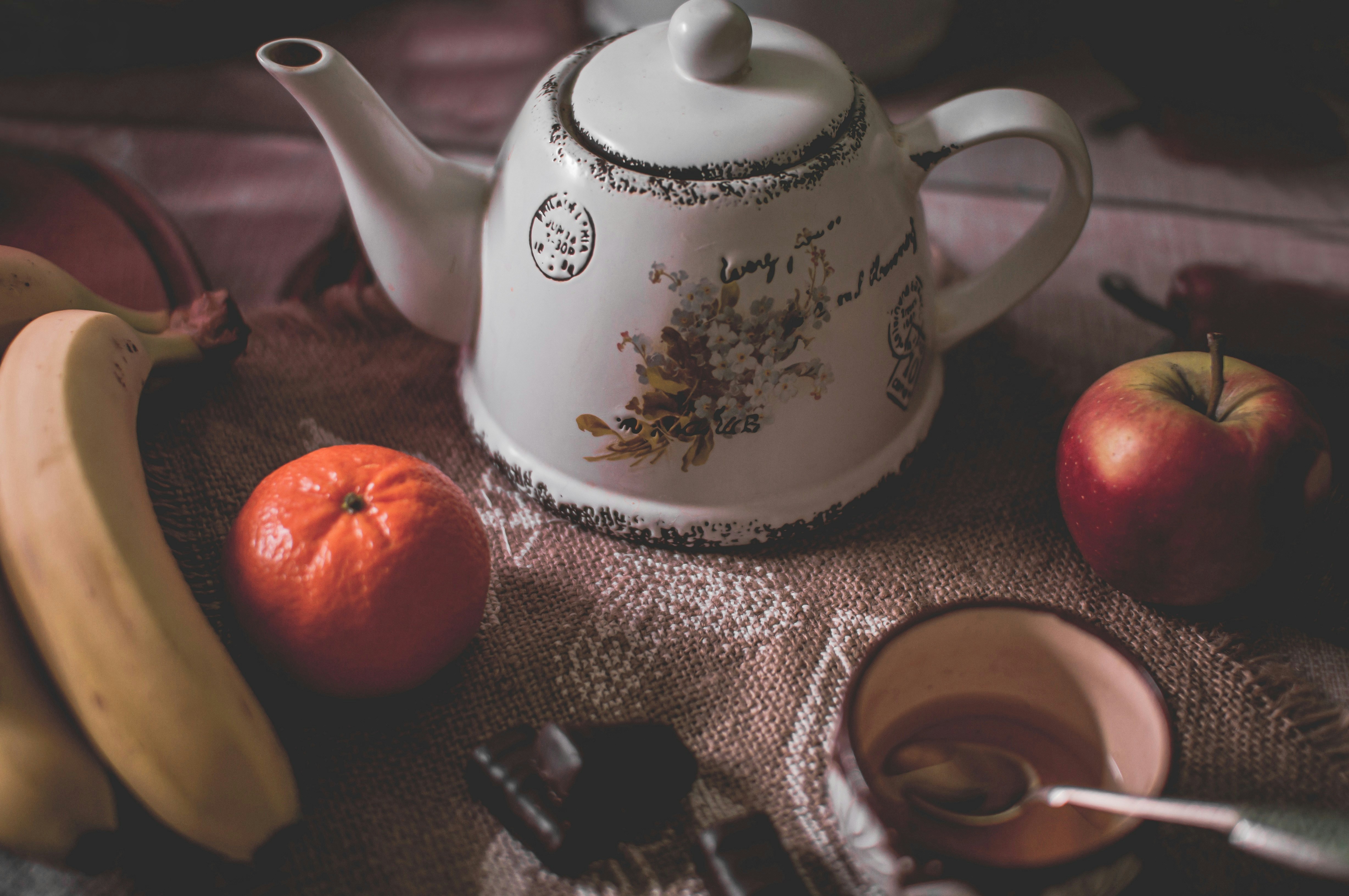 a tea pot sitting on top of a table filled with fruit