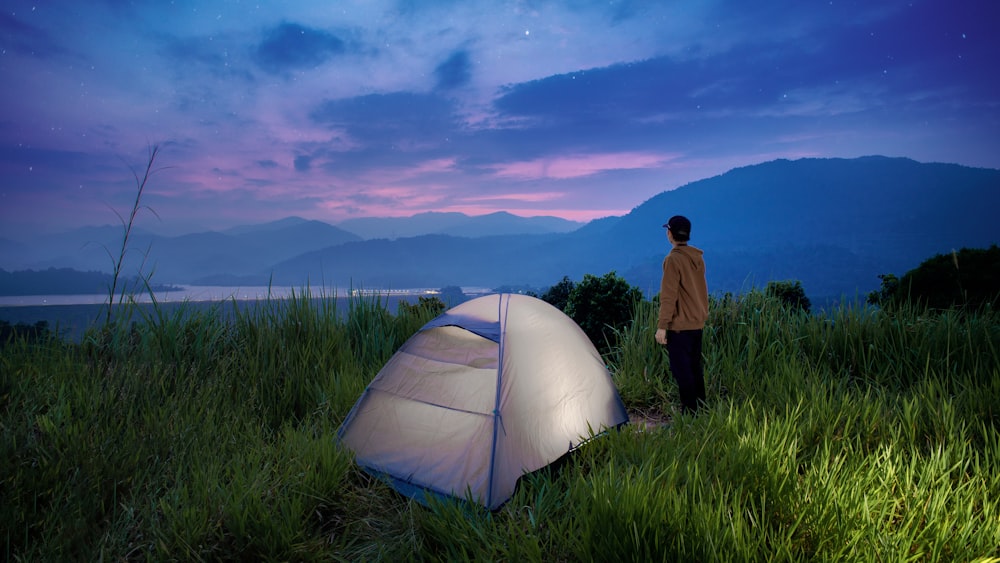 a man standing next to a tent on a lush green field