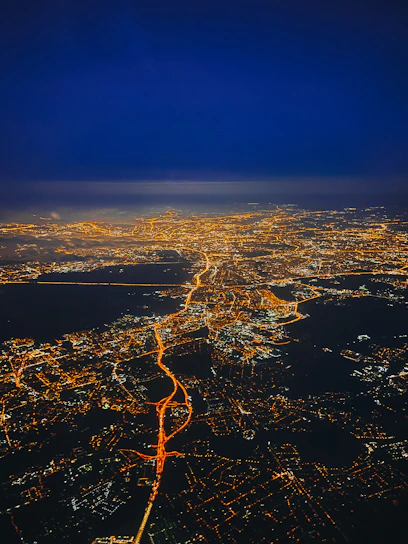 A sleek aerial view of a logistics hub at night, illuminated with precise white and orange lights symbolizing data flow and operational agility.