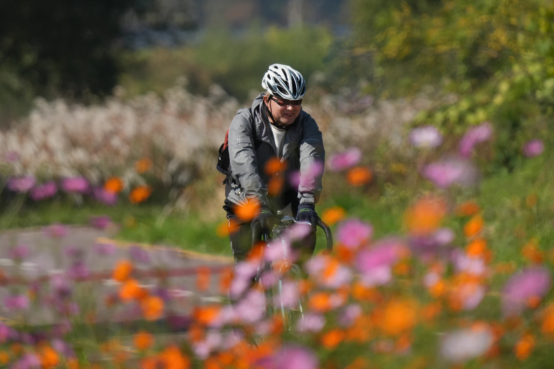 Close-up of a cyclist's hands gripping the handlebars, with a blurred background of colorful wildflowers along the route.