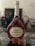 A bottle of Mateus Rosé wine with a uniquely shaped, elegant glass bottle. The label features the words 'Mateus The Original Rosé Portugal' along with an illustration of an estate. The bottle is on a glass table with decorative stones underneath, and the background is slightly blurred.