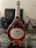 A bottle of Mateus Rosé wine with a uniquely shaped, elegant glass bottle. The label features the words 'Mateus The Original Rosé Portugal' along with an illustration of an estate. The bottle is on a glass table with decorative stones underneath, and the background is slightly blurred.