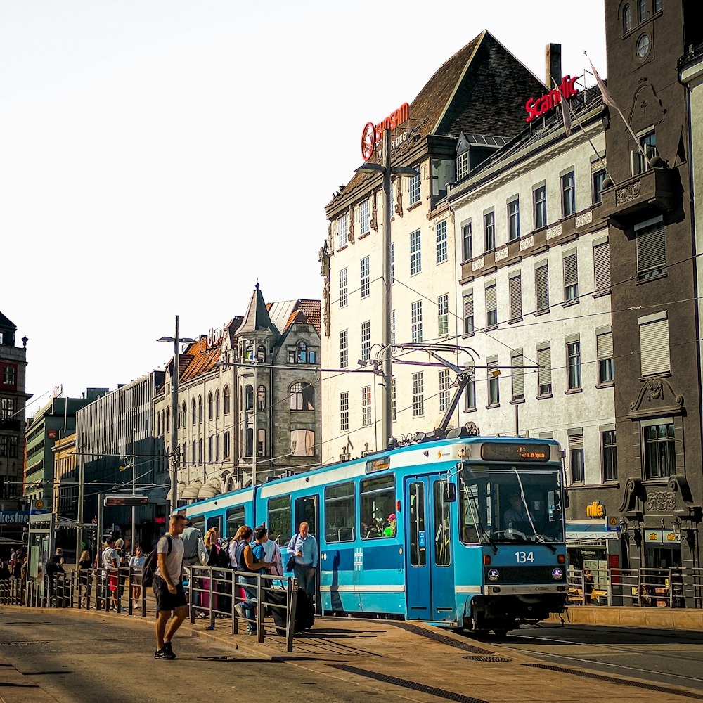 a blue train traveling down a street next to tall buildings