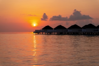 A tropical Maldives overwater bungalow at sunset with calm waters reflecting the colorful sky.