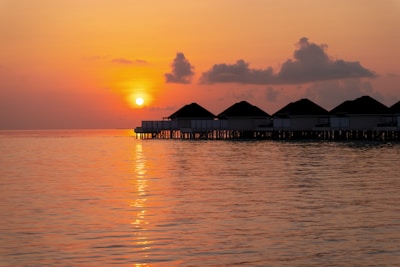 A tropical Maldives overwater bungalow at sunset with calm waters reflecting the colorful sky.