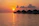 A smiling woman relaxing on the deck of an overwater villa at sunset with the ocean glowing behind her.