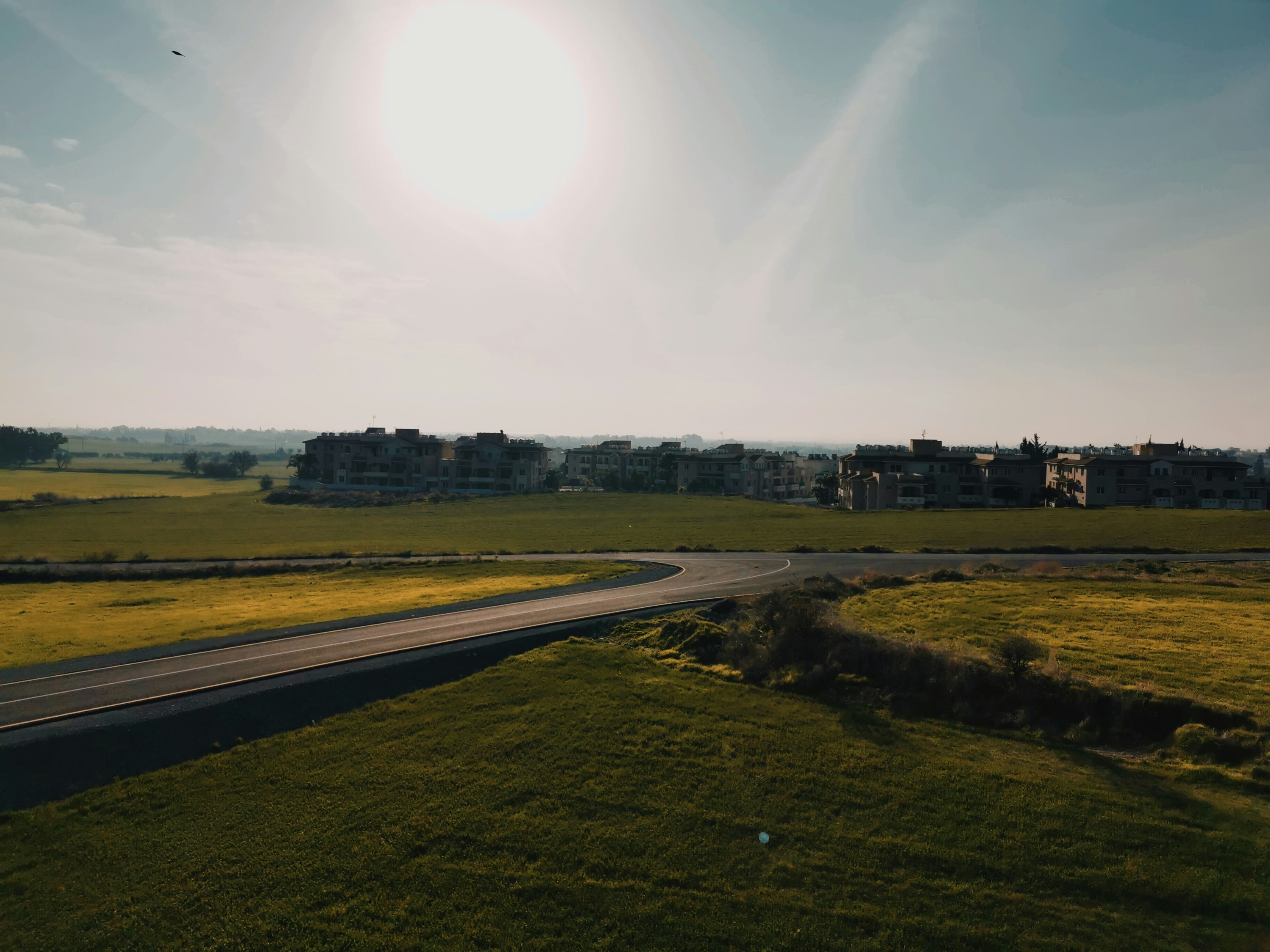 the sun is shining over a road in the middle of a field
