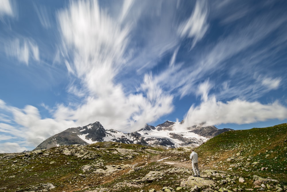 a person standing on a rocky hillside with a mountain in the background