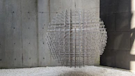 A minimalist sculpture of intertwined metal rods casting delicate shadows on a white wall.