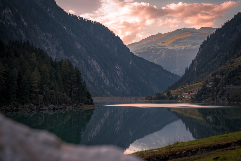 a lake surrounded by mountains under a cloudy sky