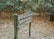 A wooden sign in a wooded area with fallen leaves. The sign reads 'Entering a Sanctuary', 'Plants and Animals', 'Strictly Protected'. Trees and dense foliage surround the path.