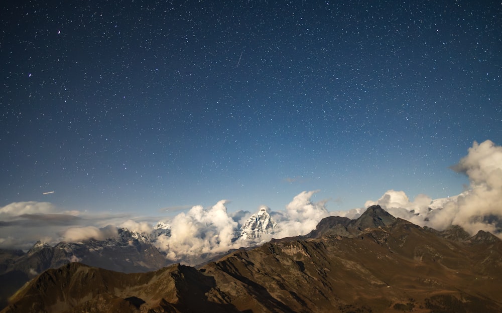 the night sky over a mountain range with clouds and stars