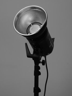 A studio light mounted on a stand with a large reflective dish and a cylindrical body. The setup is simple and focuses on the lighting equipment against a plain background.