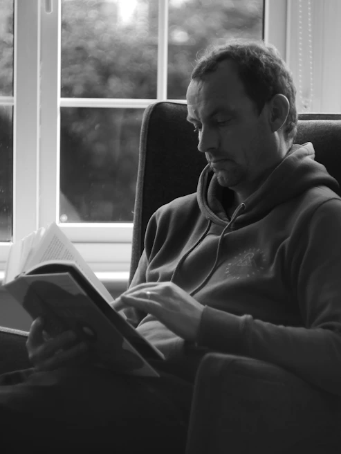 A minimalist black and white photo of a man reading a book in a dimly lit room