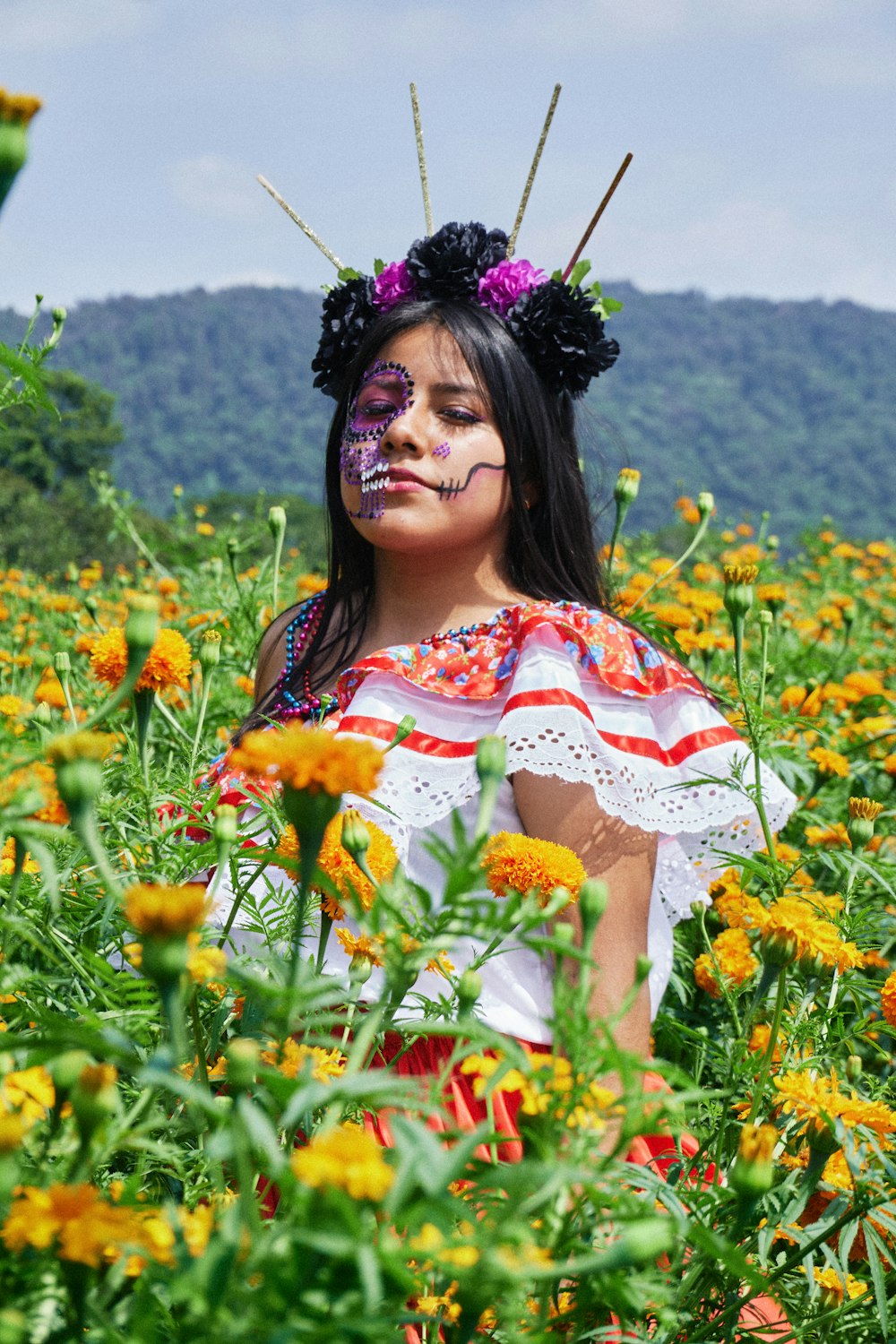 a woman with face paint sitting in a field of flowers