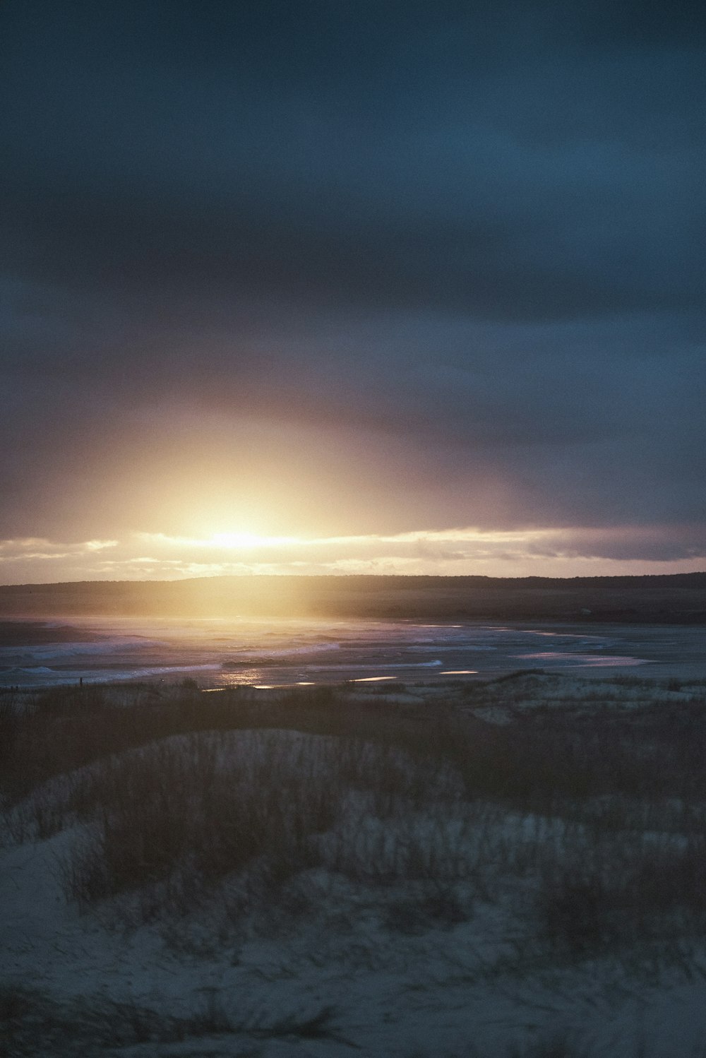 the sun is setting over the ocean on a cloudy day