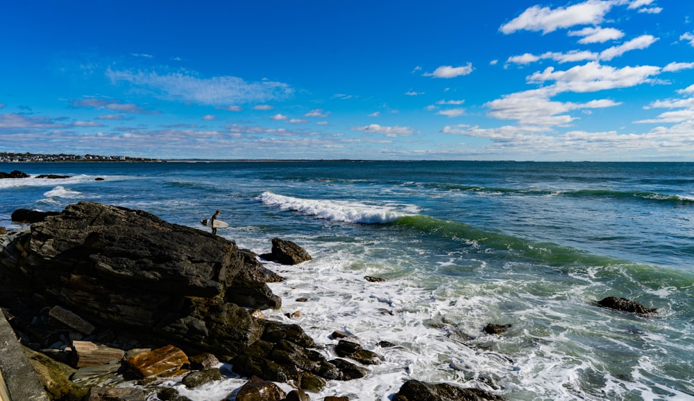 a person standing on a rocky shore next to the ocean