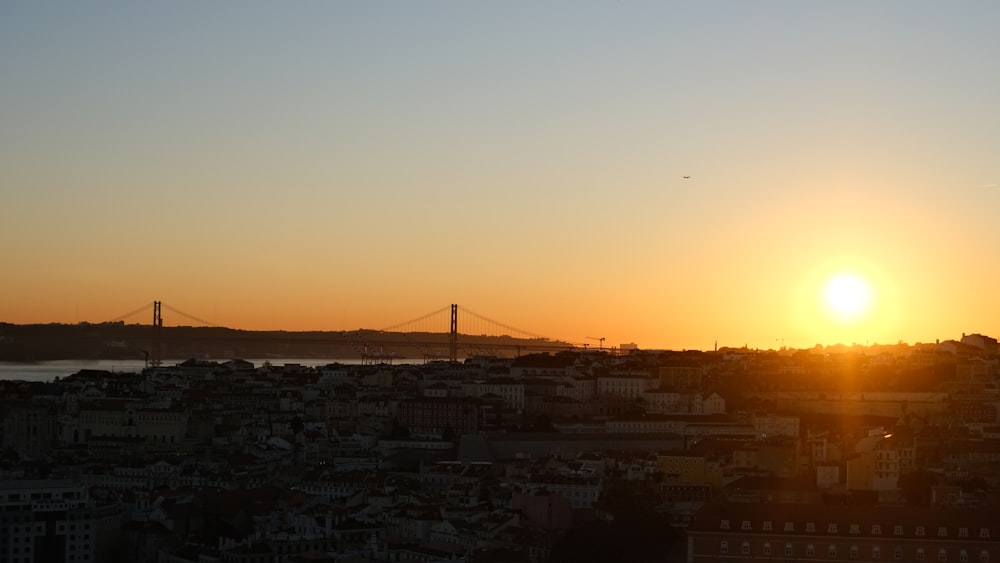 the sun setting over a city with a bridge in the background