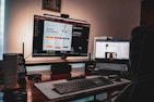 A dimly lit workspace featuring a desktop monitor displaying a website development page and a laptop showing a digital growth insights page. The setup includes a keyboard, mouse, two cups, a pen holder, and a clock displaying '02 36'. The atmosphere suggests a cozy, focused work environment.