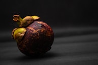 A vibrant mangosteen fruit resting beside a cup of coffee on a wooden table.