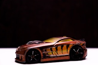 A toy car with a sleek design, featuring a bronze color and black wheels. The car is adorned with black and yellow stripe detailing on the side, resembling claw marks. It is photographed against a dark background.
