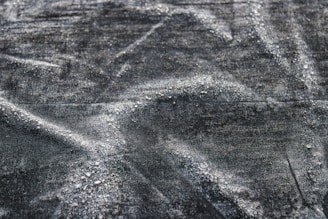 A close-up texture of dark fabric with visible water droplets creating a pattern across the surface. The material appears to be slightly wrinkled, adding depth and interest to the image.