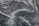 A close-up texture of dark fabric with visible water droplets creating a pattern across the surface. The material appears to be slightly wrinkled, adding depth and interest to the image.