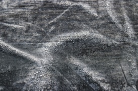 A close-up texture of dark fabric with visible water droplets creating a pattern across the surface. The material appears to be slightly wrinkled, adding depth and interest to the image.