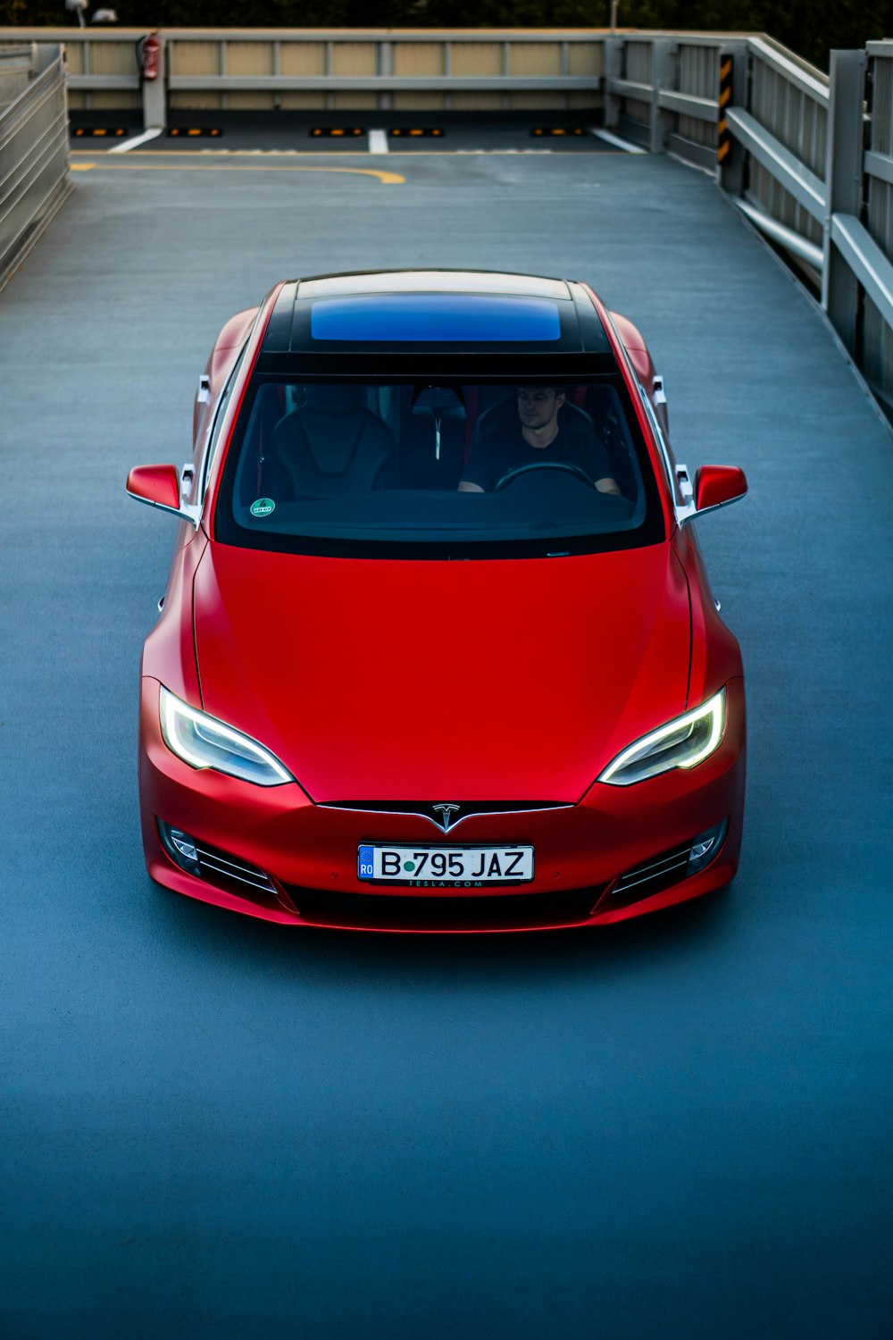 a red car driving down a road next to a bridge