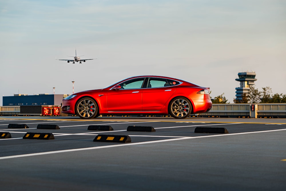 a red car on a runway with an airplane in the background