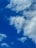 A commercial airplane flying high in the sky surrounded by scattered white clouds against a vibrant blue backdrop.